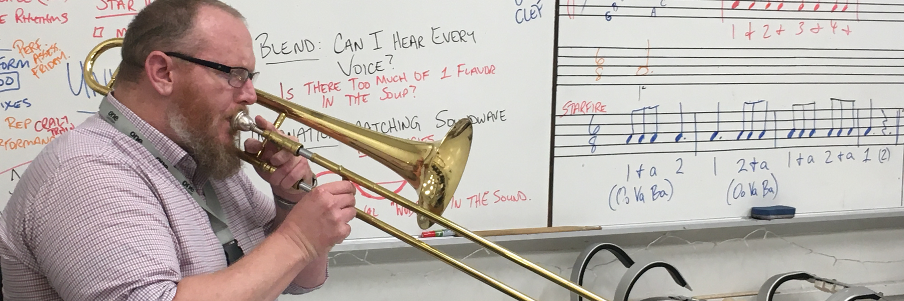 Man (Zach Wills) plays trombone in front of a whiteboard